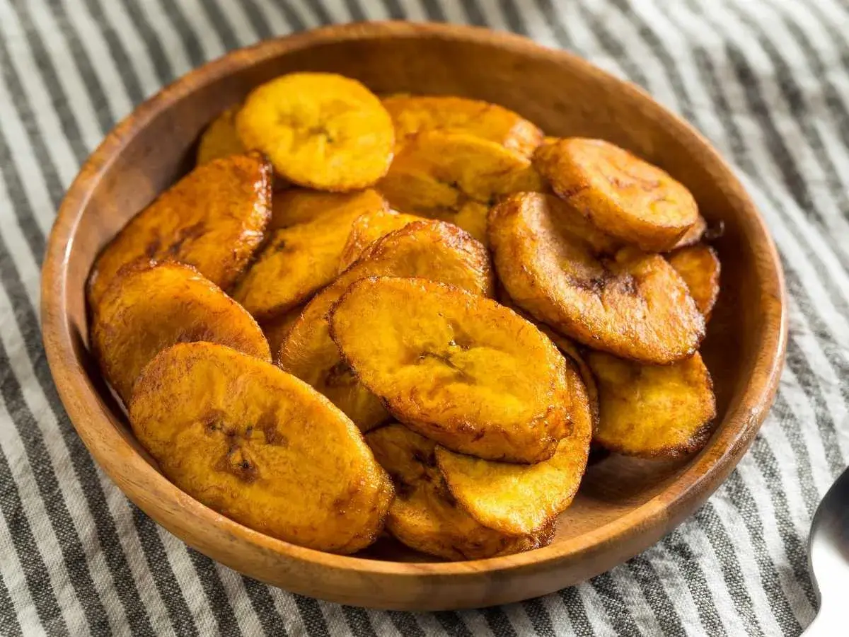 Un tazón de madera lleno de crujientes rodajas de plátano frito, doradas y listas para disfrutar.