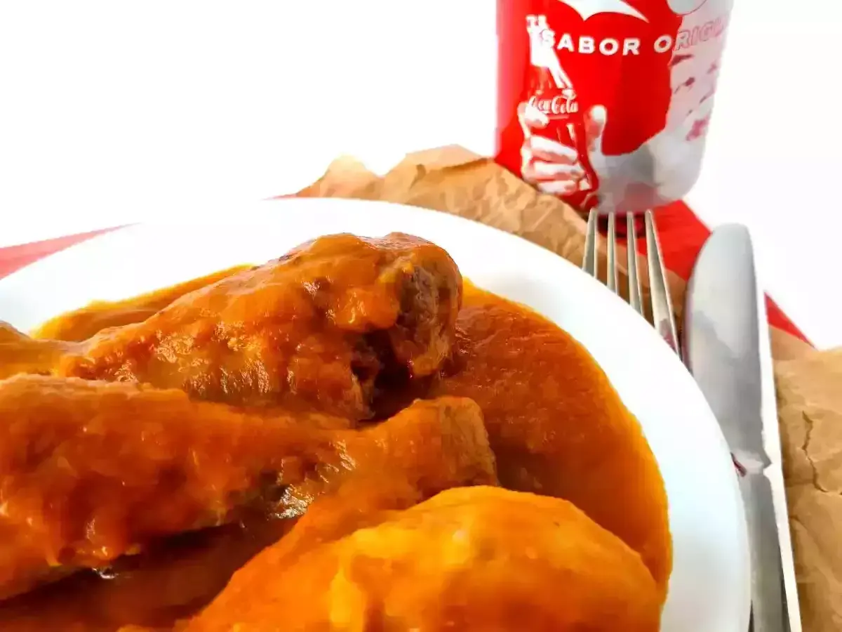 Sabroso pollo a la Coca Cola en un plato blanco, acompañado de cubiertos y una lata de Coca Cola.