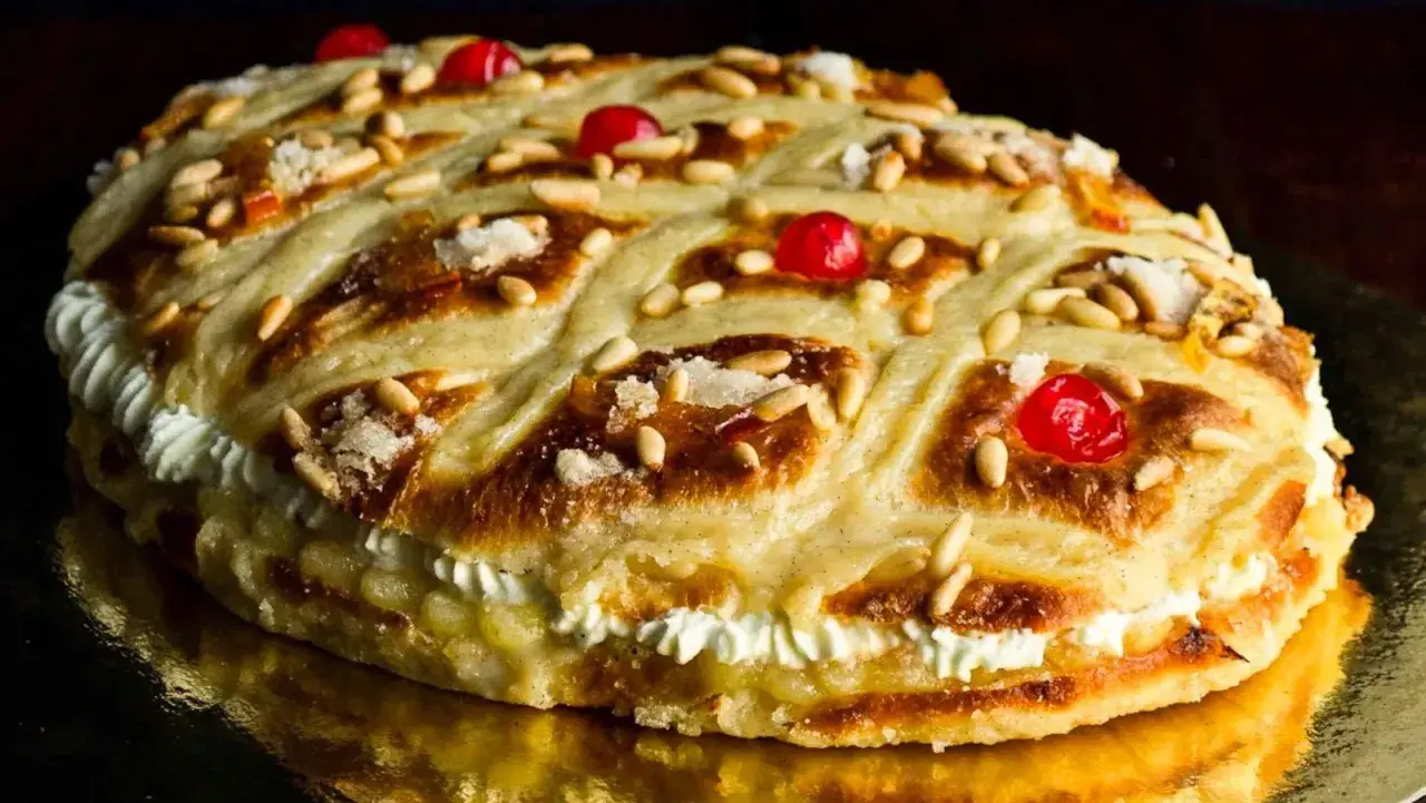 Deliciosa coca de Sant Joan rellena de crema, decorada con piñones, cerezas rojas y azúcar.