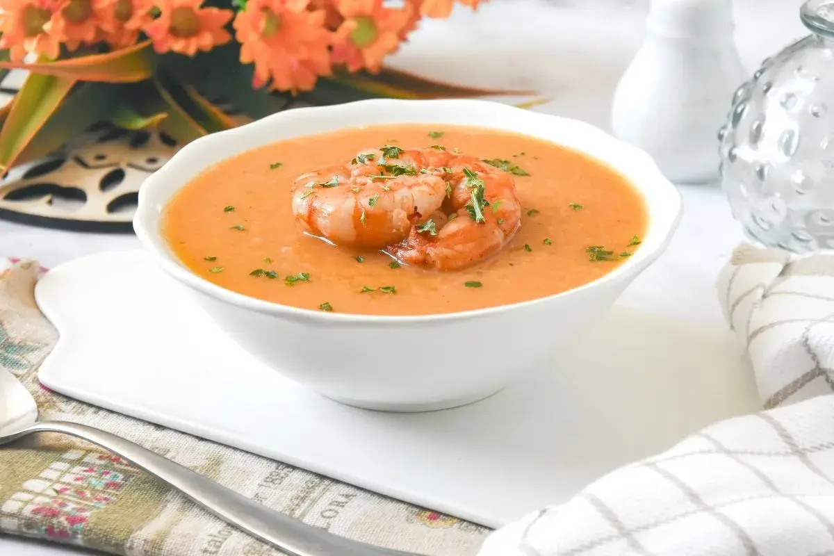 Deliciosa crema de marisco servida en un cuenco blanco, coronada con gambas y perejil picado.