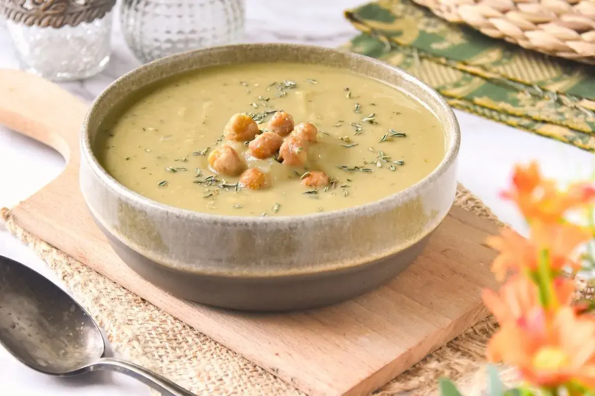 Un tazón de cremosa crema de garbanzos, decorada con garbanzos enteros y hierbas, servida en una tabla de madera.