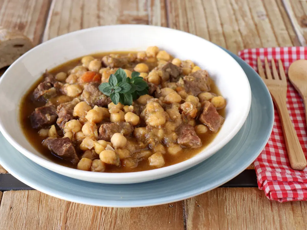 Un plato humeante de garbanzos con carne, perfecto para una receta de garbanzos tradicional. Decorado con una ramita de hierbas frescas.
