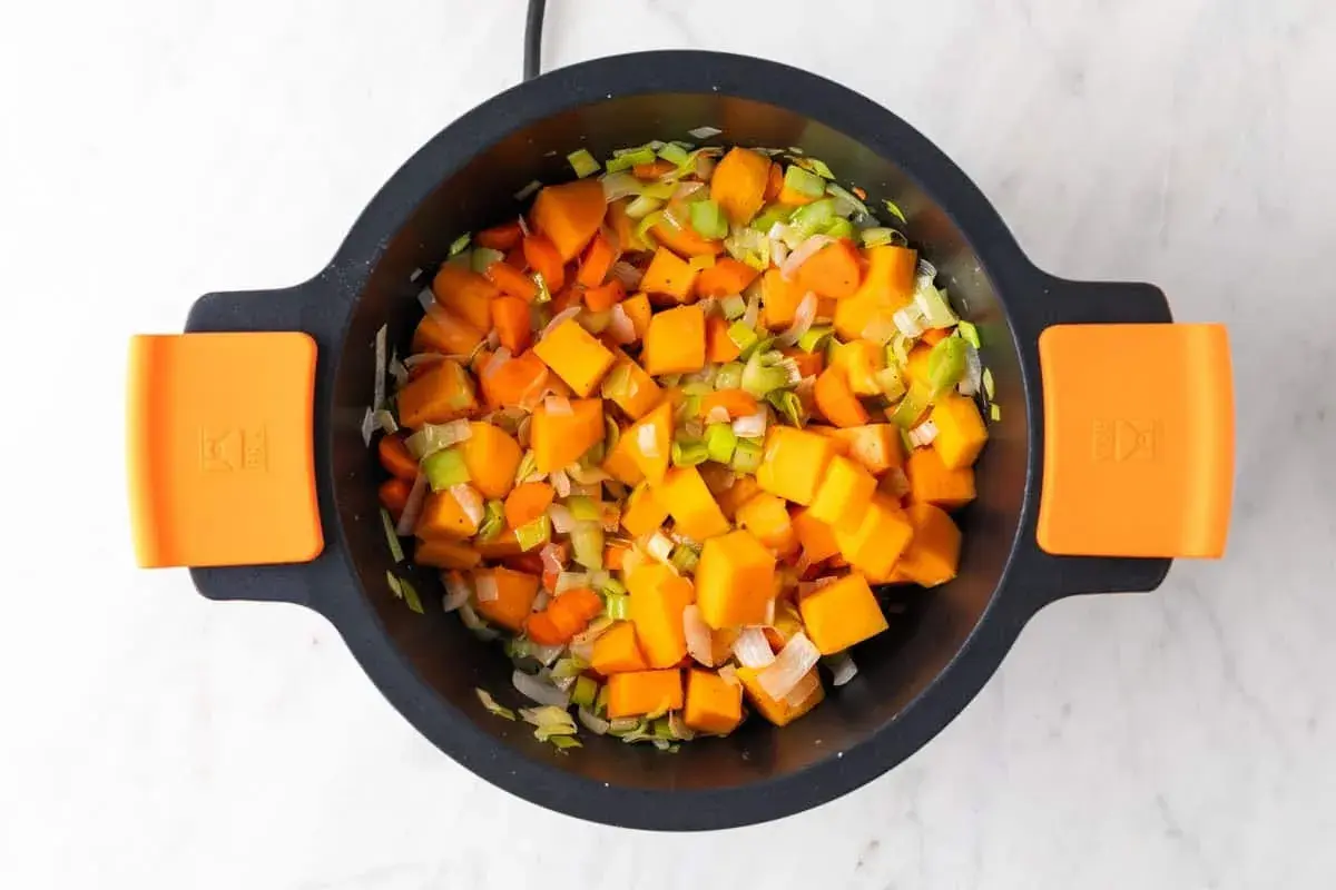 Trozo de calabaza, zanahoria y puerro picados en una olla, listos para hacer una deliciosa crema de verduras.