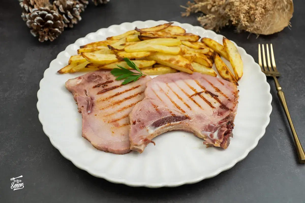Dos chuletas de sajonia a la parrilla con patatas fritas y perejil en un plato blanco.