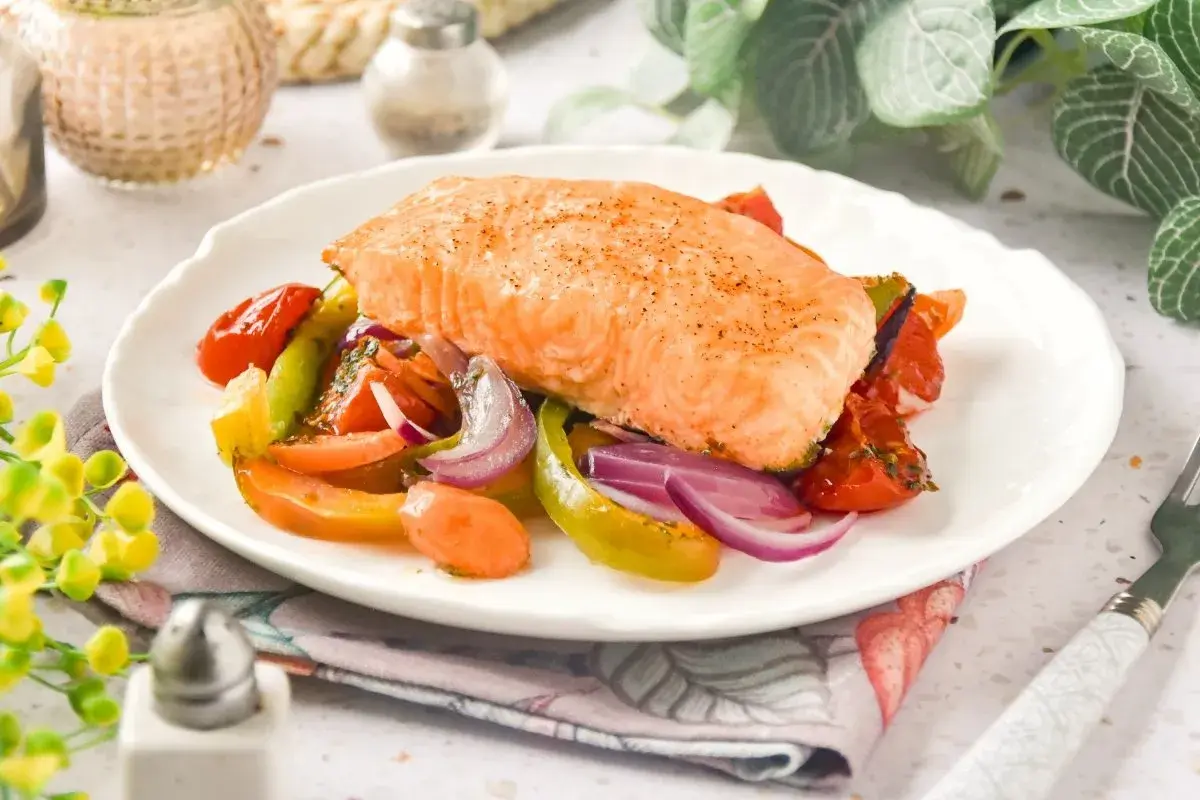 Delicioso salmón al horno con verduras coloridas: tomates, pimientos y cebolla morada. Un plato saludable y lleno de sabor.