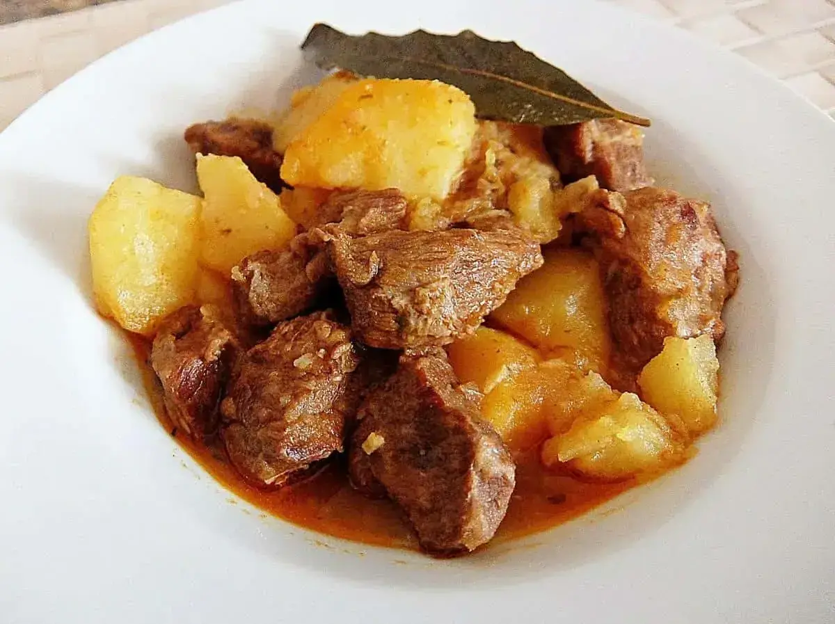 Plato de morcillo de ternera estofado con patatas y una hoja de laurel.