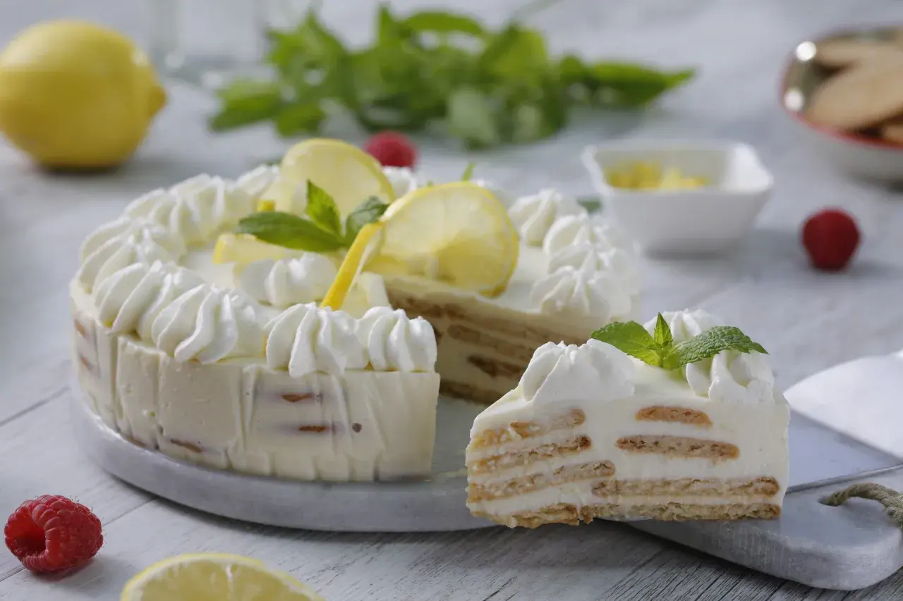 Deliciosa tarta de limón sin horno, con capas de galleta y crema, decorada con merengue, rodajas de limón y menta.
