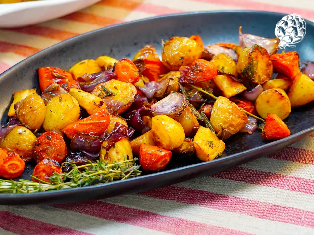 Un plato de verduras al horno, con patatas, zanahorias y cebolla morada, adornado con romero fresco.