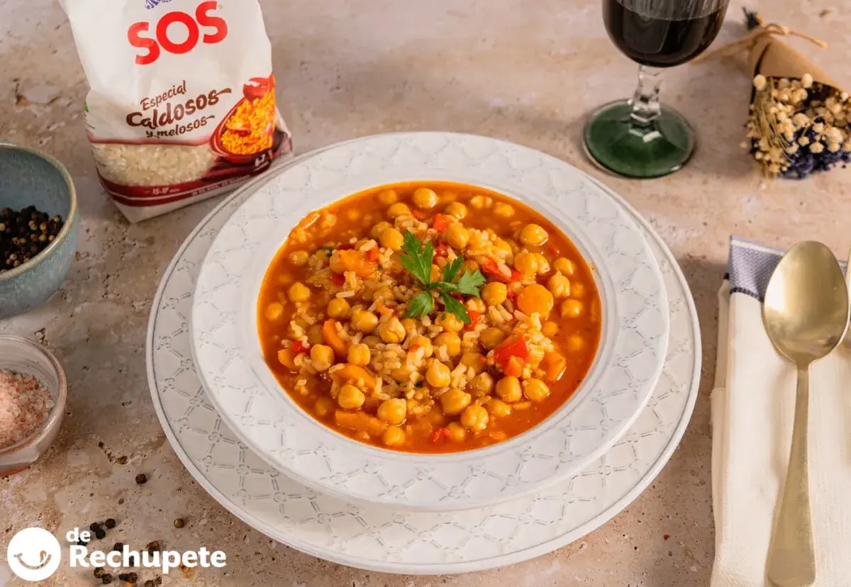 Plato de garbanzos con arroz, pimientos y zanahoria, decorado con perejil. Acompañado de una copa de vino tinto y una bolsa de arroz SOS.