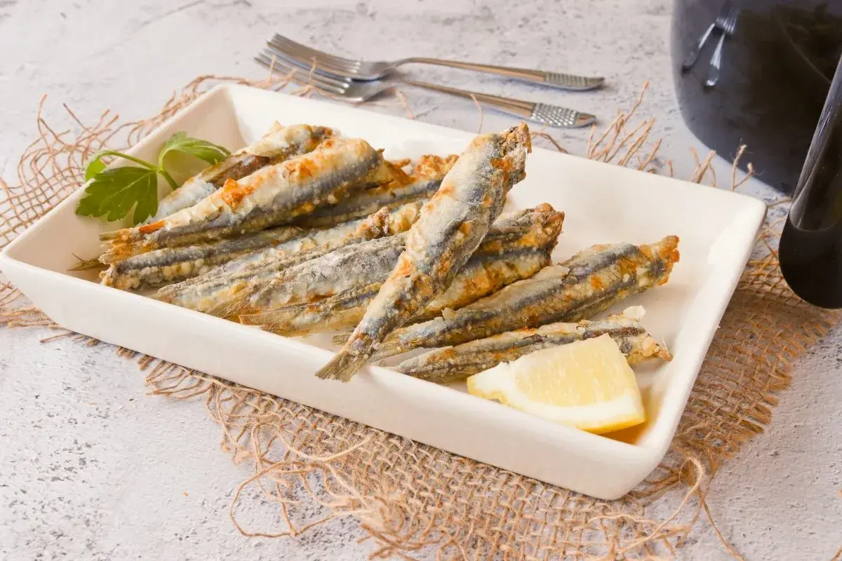 Boquerones crujientes en freidora de aire, servidos en plato blanco con limón y perejil.