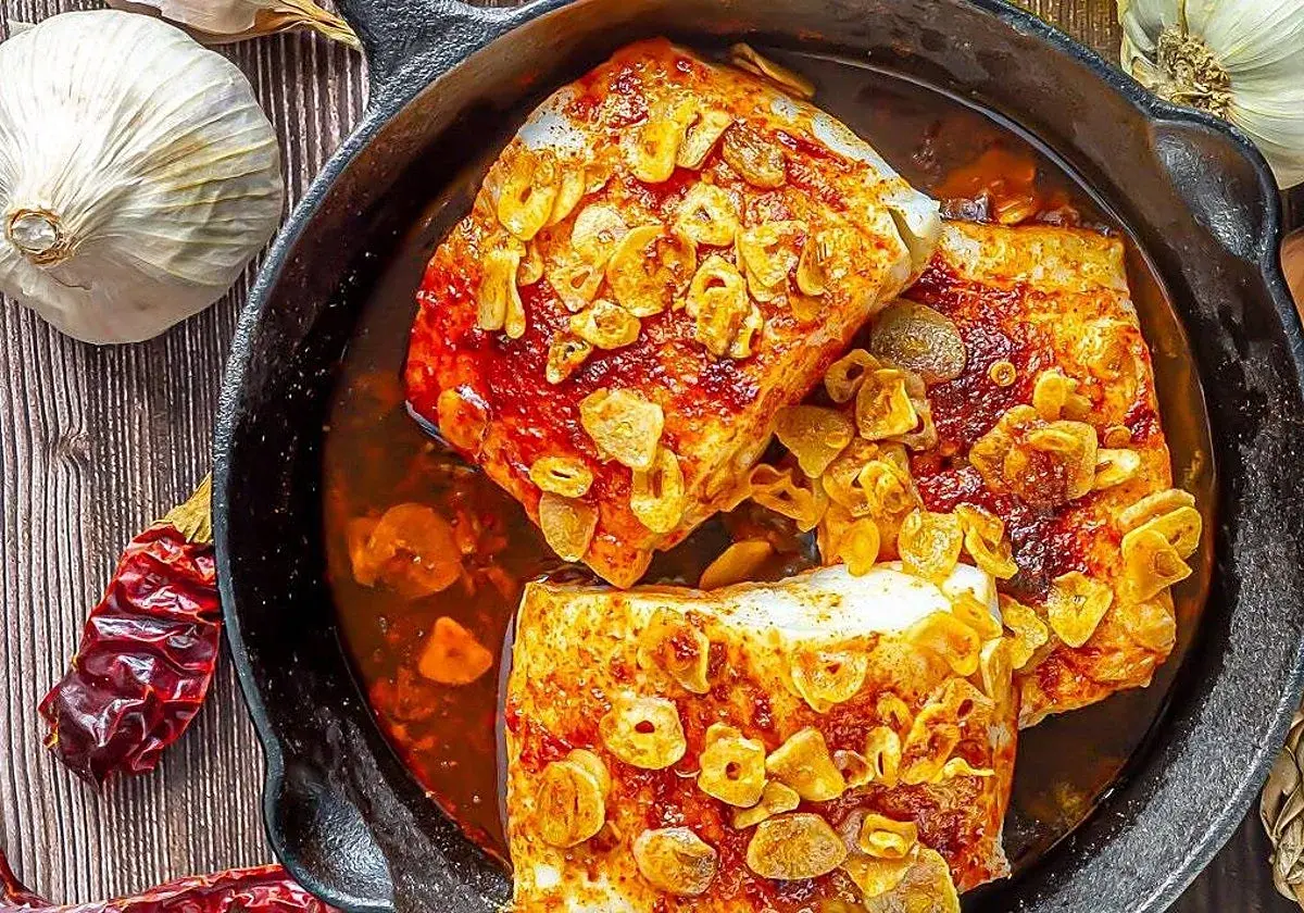 Bacalao ajoarriero en cazuela de hierro fundido, con ajos laminados dorados y guindillas secas.