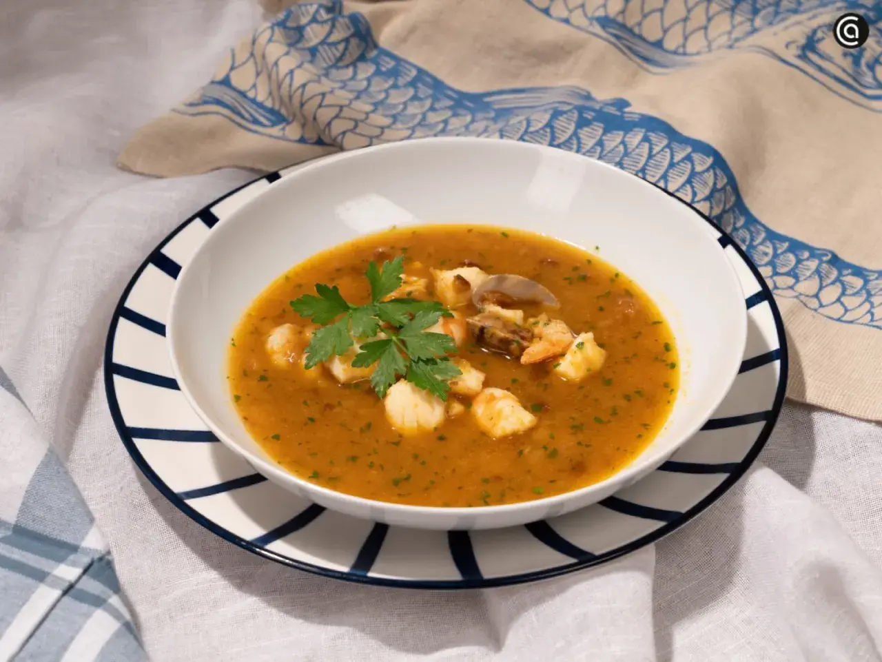 Un plato de sopa de pescado con trozos de marisco, gambas y mejillones, decorado con perejil fresco.