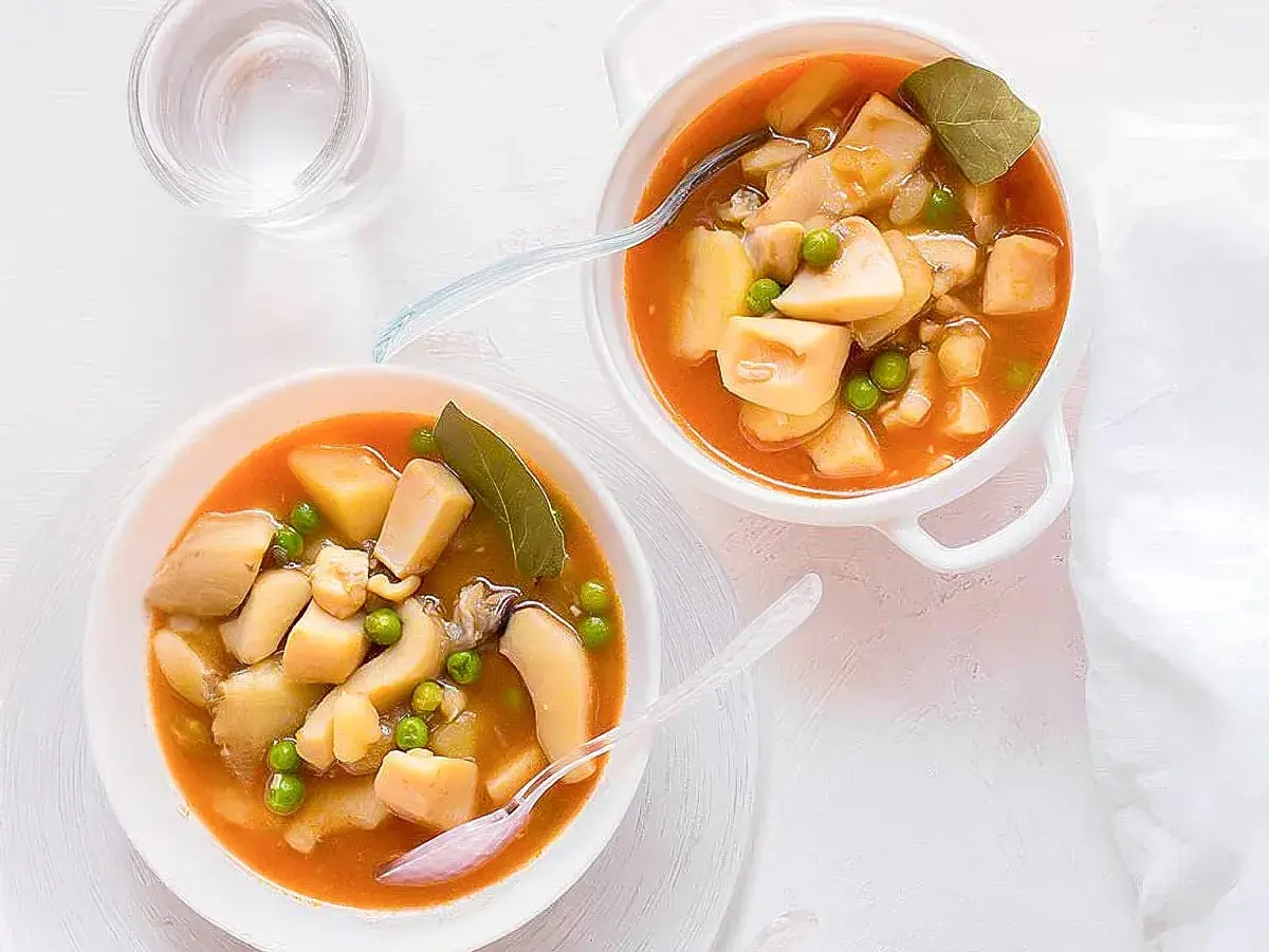 Dos cuencos de sepia con patatas y guisantes en salsa. Un vaso de agua al lado.