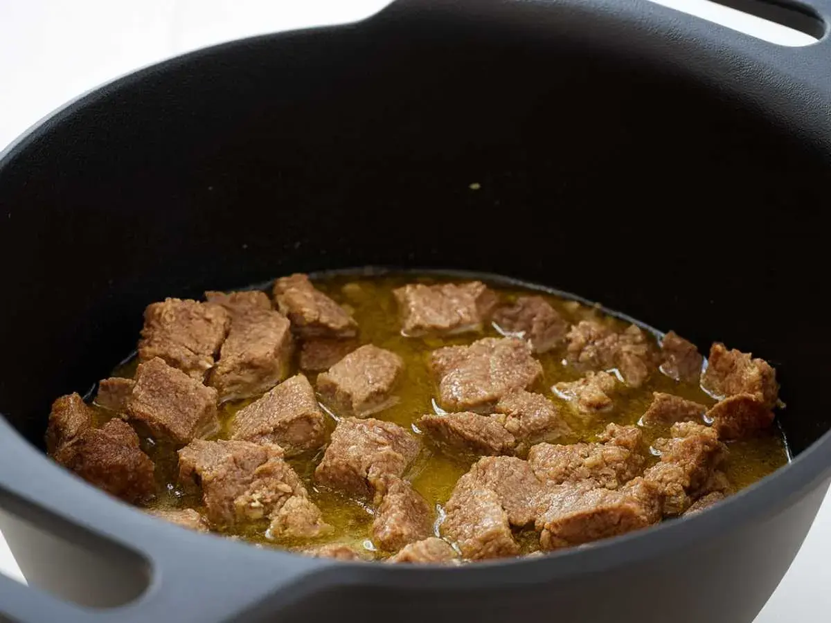 Trozos de magro con tomate cocinándose en una olla negra.