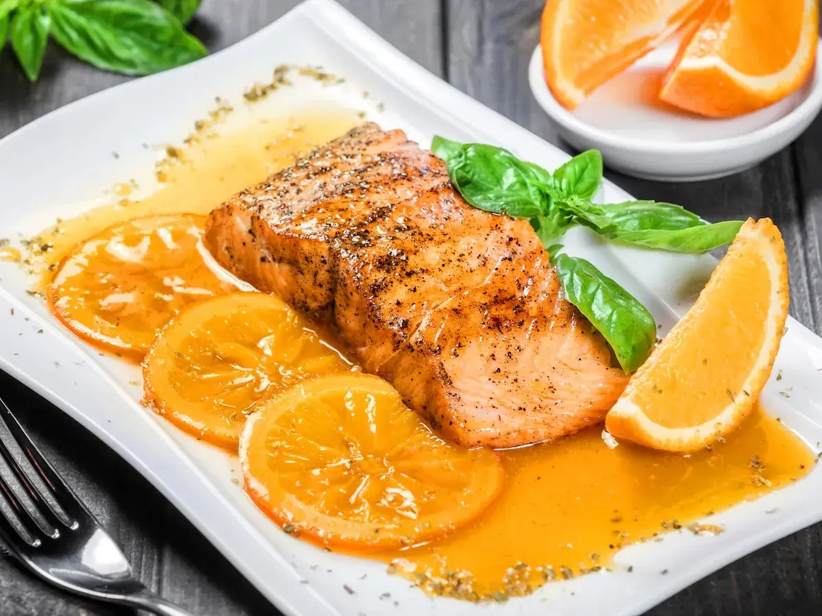 Delicioso salmón a la naranja, servido con rodajas de naranja y hojas de albahaca fresca.