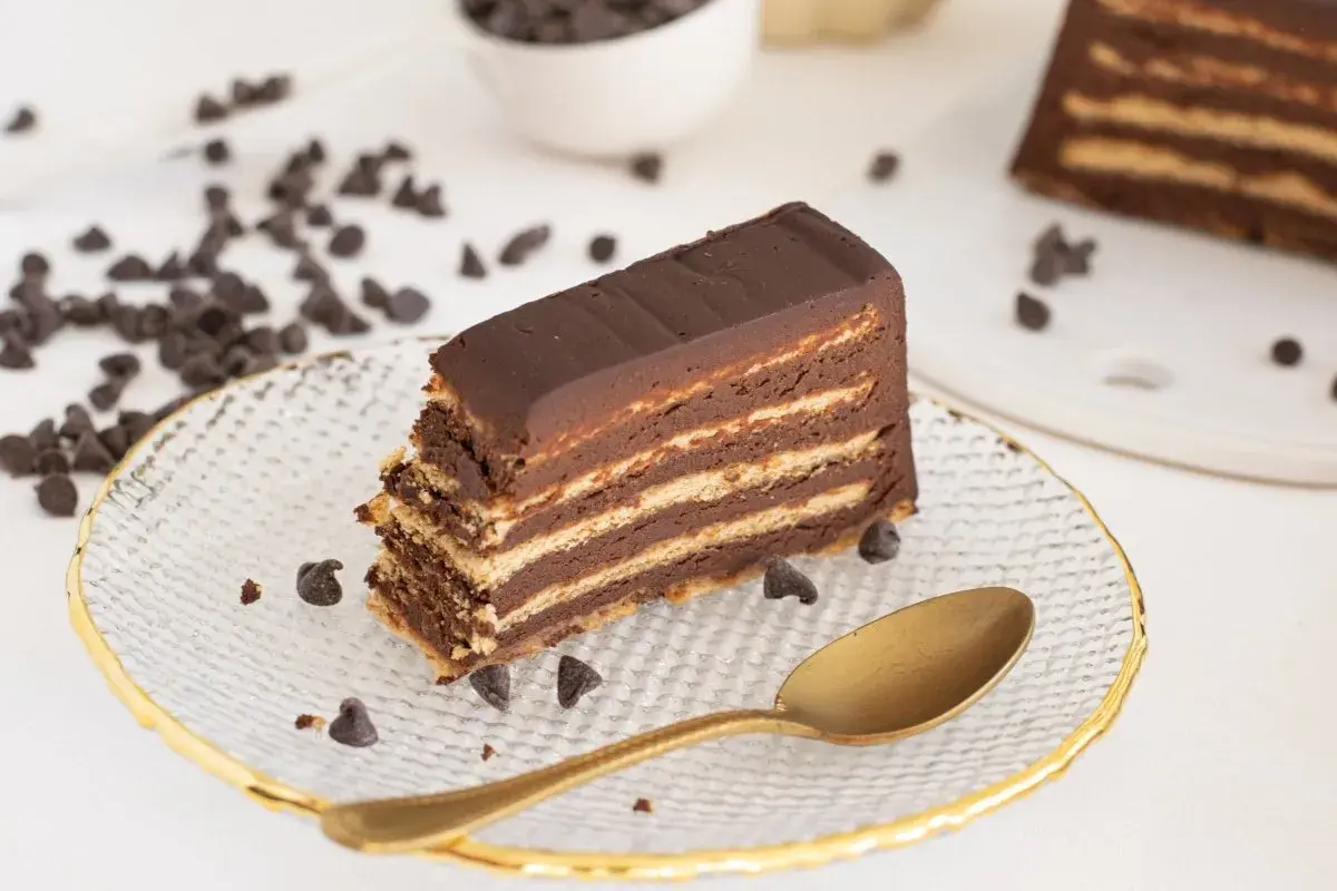 Rebanada de tarta de galletas de la abuela, con capas de galleta y chocolate, decorada con chispas de chocolate y una cuchara dorada.