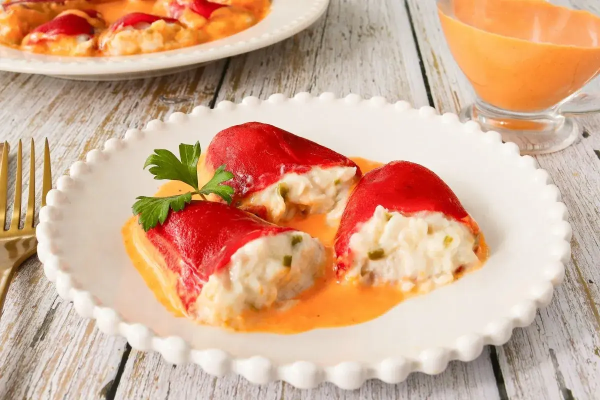 Pimientos del piquillo rellenos de bacalao, cubiertos en una cremosa salsa naranja, adornados con perejil fresco.