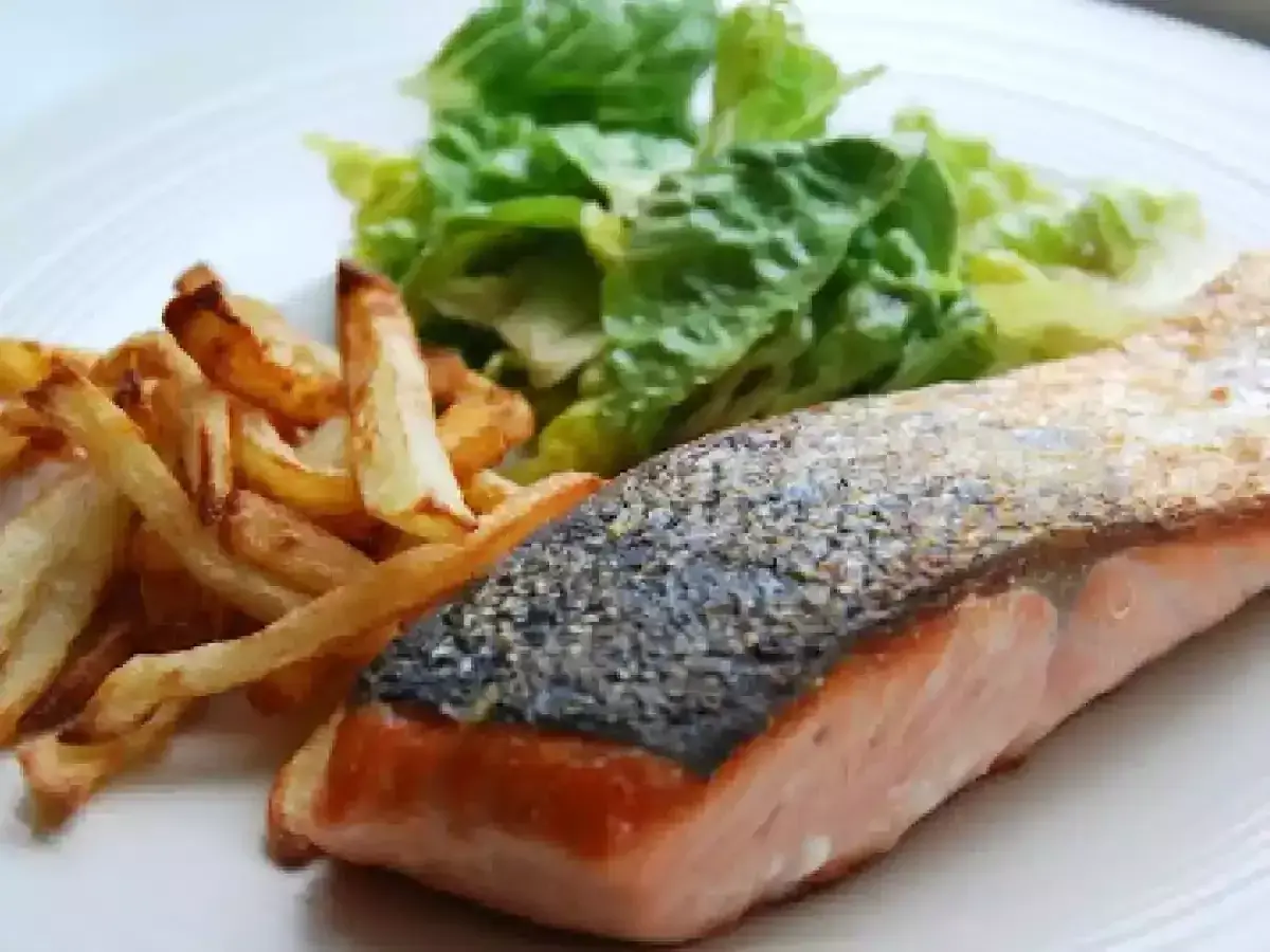 Un jugoso salmón a la plancha con piel crujiente, acompañado de patatas fritas doradas y una fresca ensalada verde.