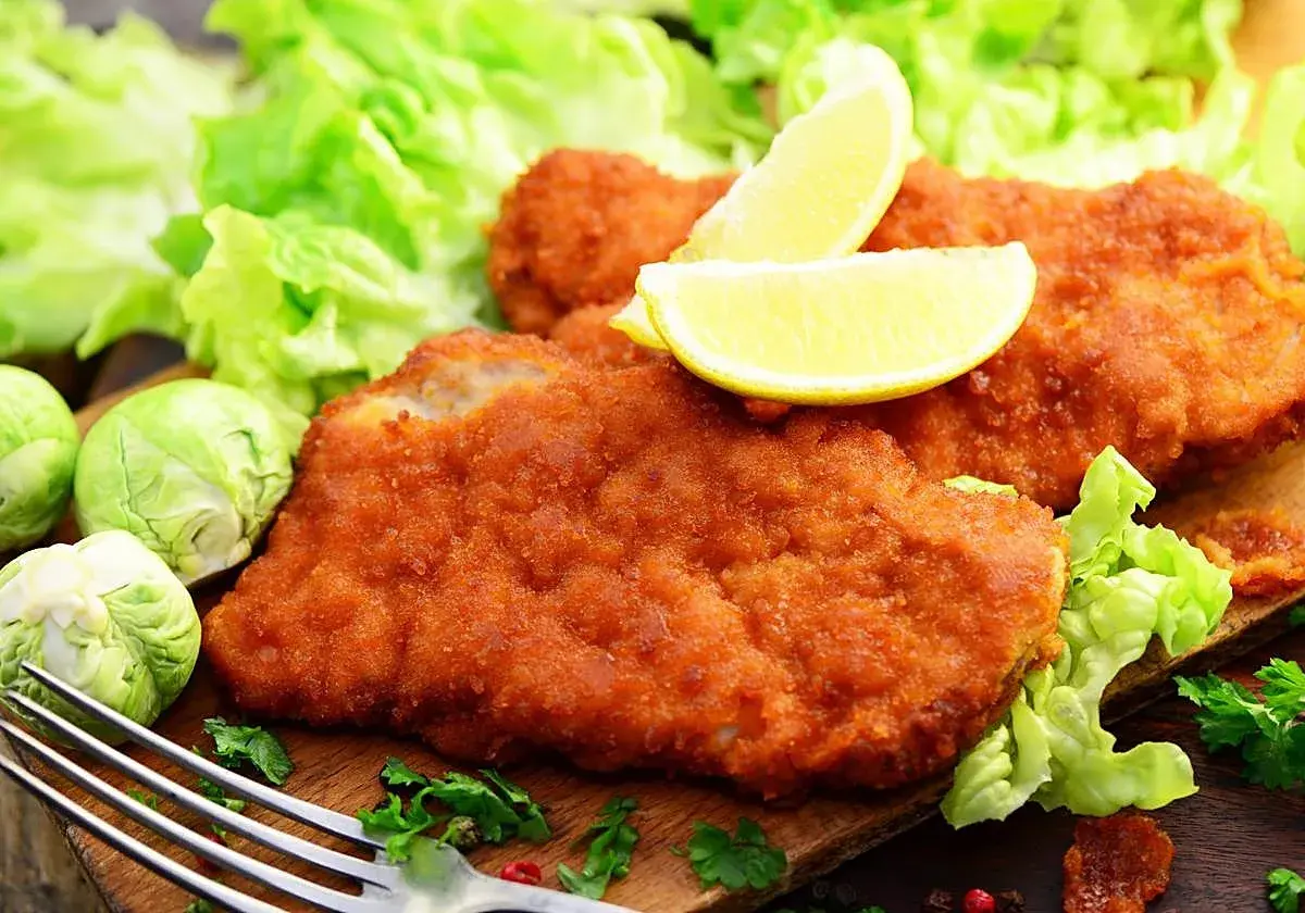 Dos filetes empanados dorados, servidos con lechuga fresca, limones y coles de Bruselas. Un plato delicioso y crujiente.