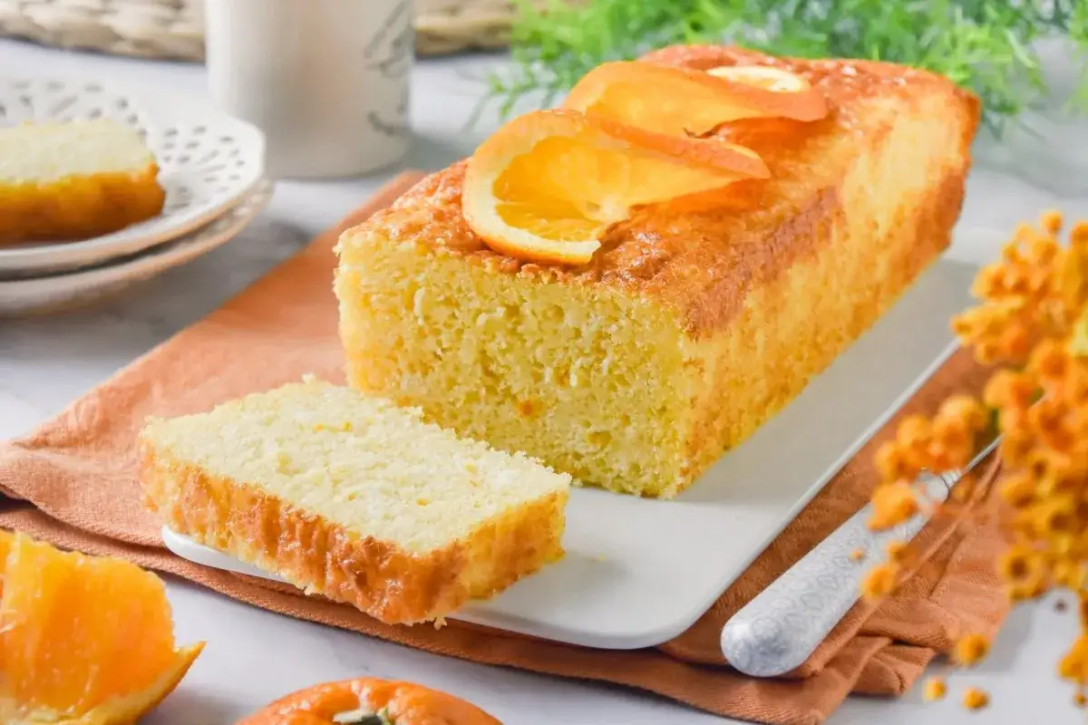 Un delicioso bizcocho de naranja, con rodajas de naranja fresca encima y una rebanada ya cortada, listo para disfrutar.
