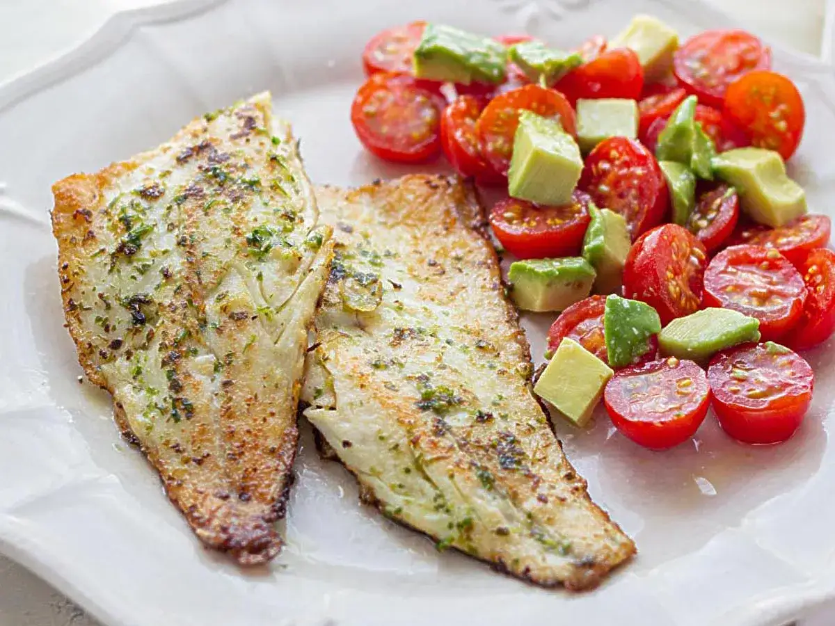 Dos filetes de lubina a la plancha con hierbas, acompa&ntilde;ados de una ensalada fresca de tomates cherry y aguacate en cubos.
