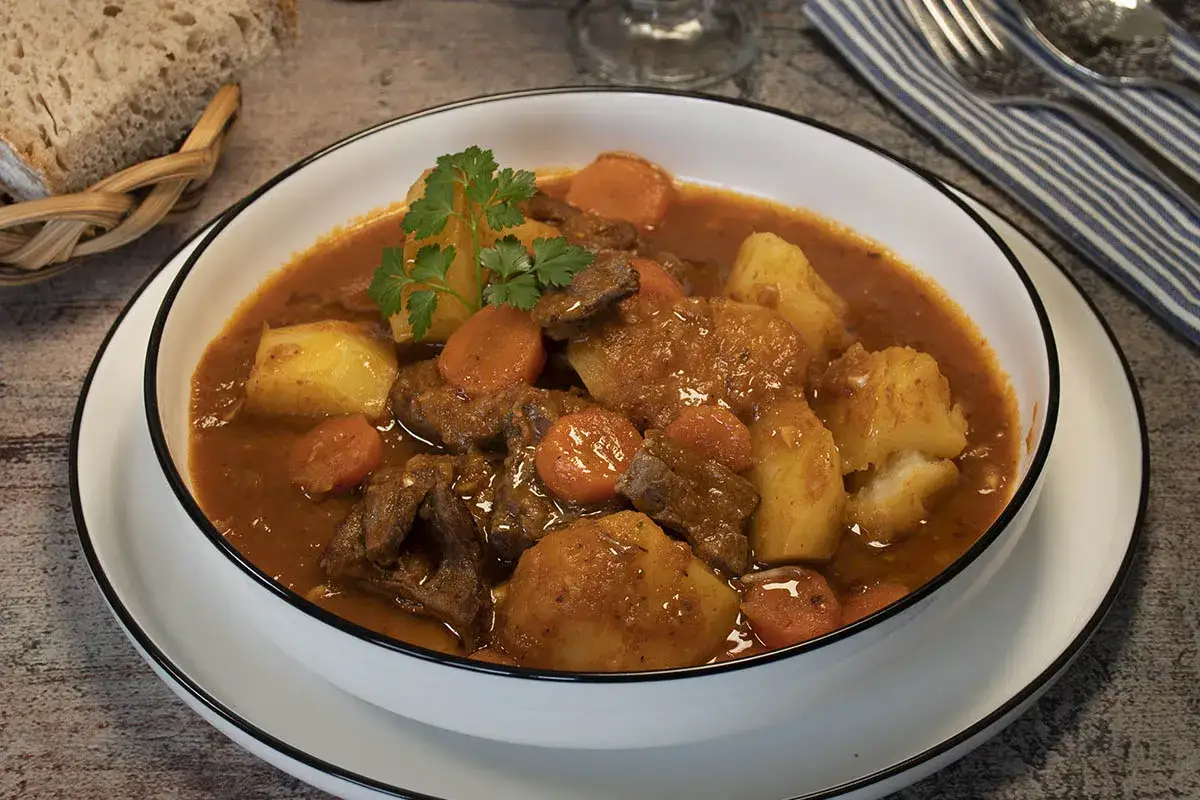 Un reconfortante plato de ternera en salsa, con trozos de patata y zanahoria, adornado con perejil fresco.