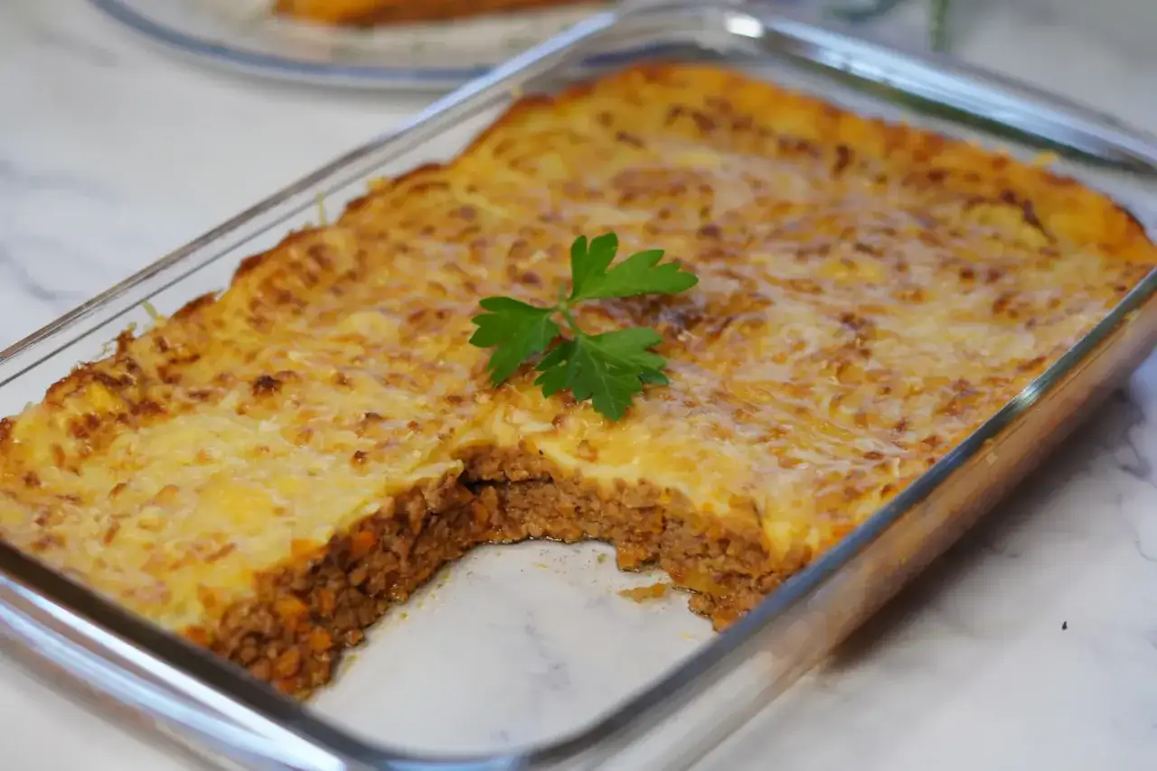 Pastel de carne picada reci&eacute;n horneado en una fuente de vidrio, con una capa dorada de queso gratinado y un toque de perejil.