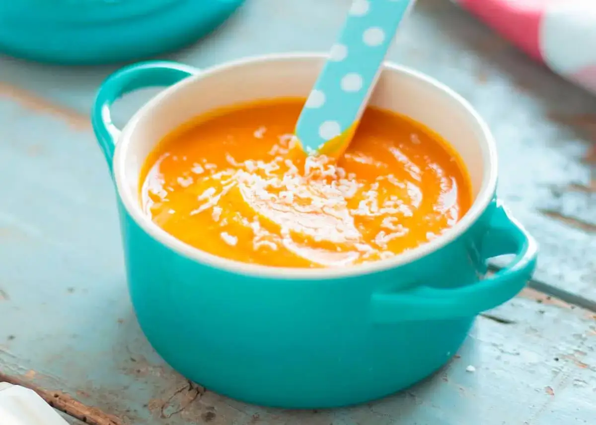 Crema de calabaza con un toque de queso rallado, servida en un cuenco turquesa con una cuchara de lunares.