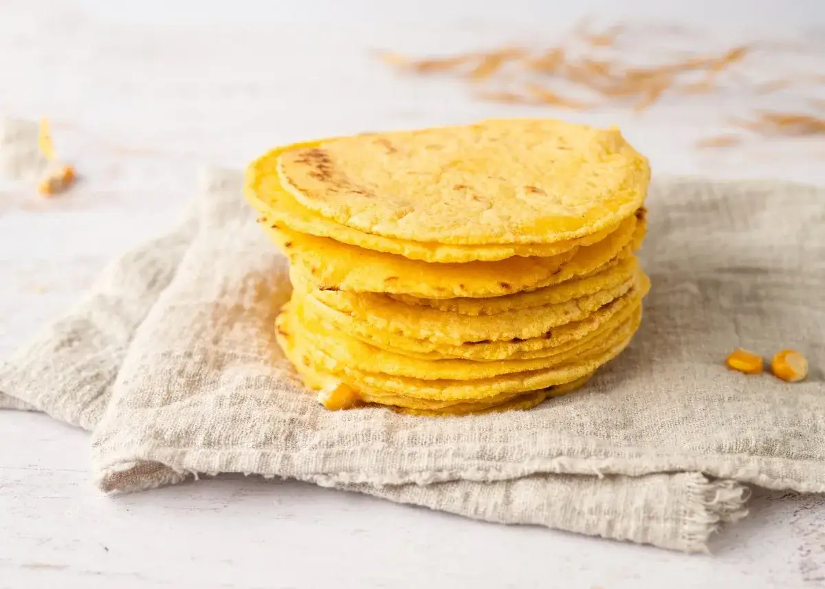 Pila de tortitas de ma&iacute;z reci&eacute;n hechas, doradas y suaves, sobre una tela r&uacute;stica. Perfectas para acompa&ntilde;ar cualquier platillo.