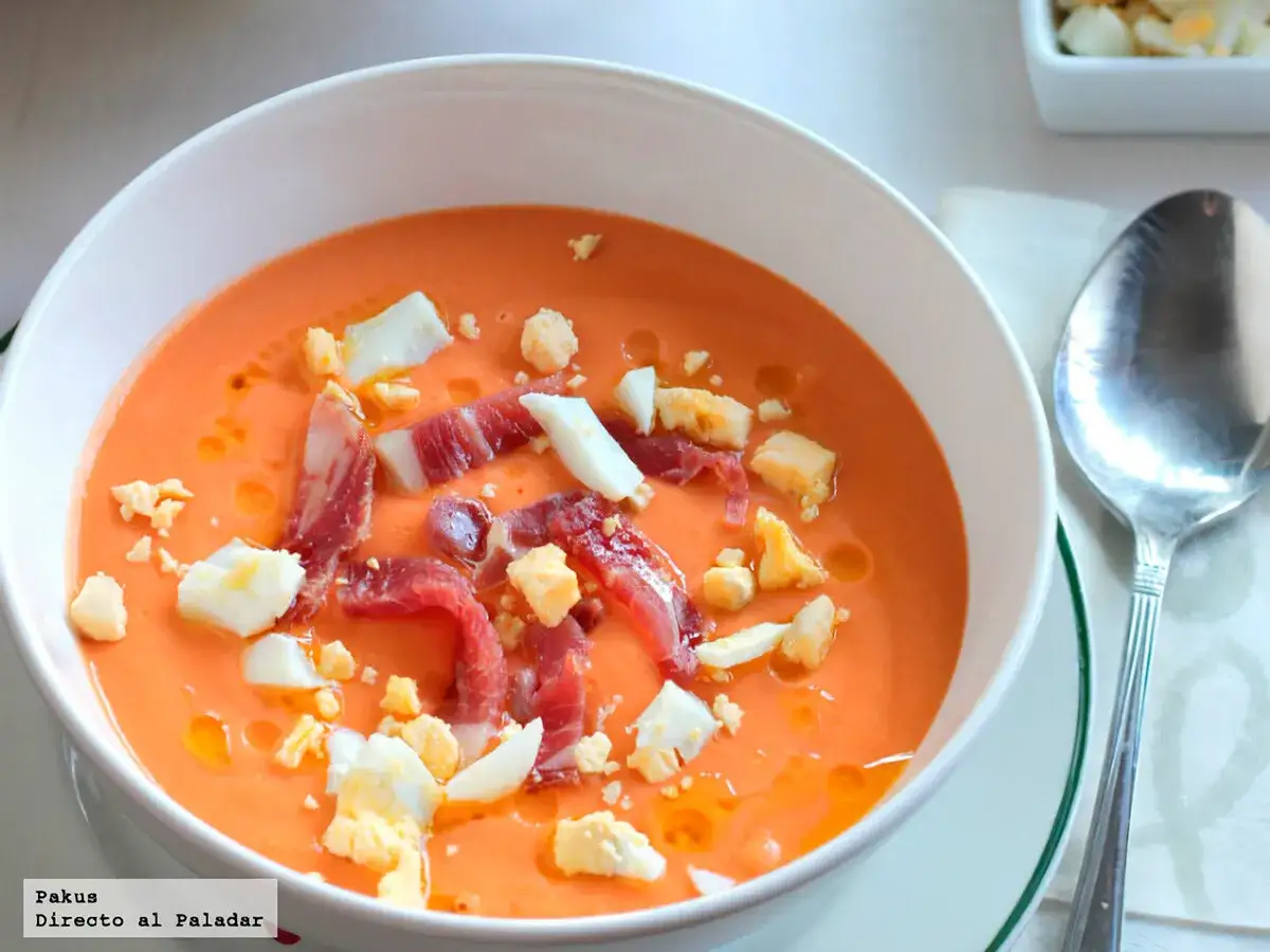 Salmorejo cremoso con jam&oacute;n serrano y huevo duro picado, mostrando los ingredientes clave de esta delicia.