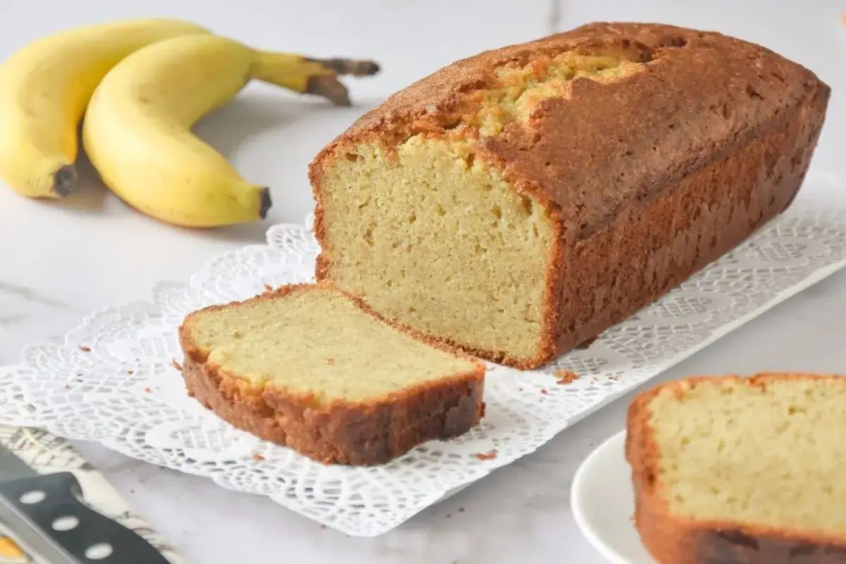 Un delicioso bizcocho de plátano sin azúcar, con una rebanada cortada y plátanos frescos al lado.