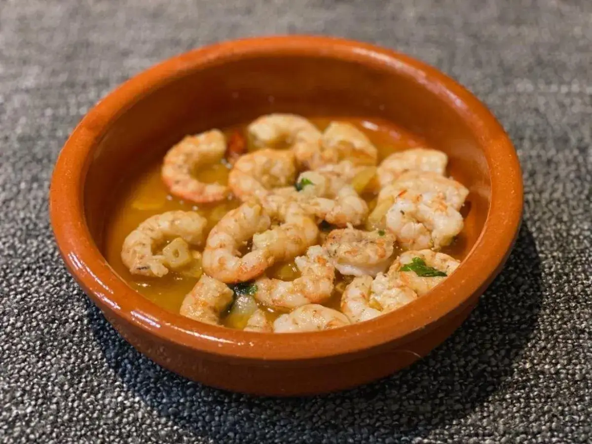 Taz&oacute;n de barro con langostinos al ajillo, jugosos y dorados, nadando en aceite de oliva con trocitos de ajo.