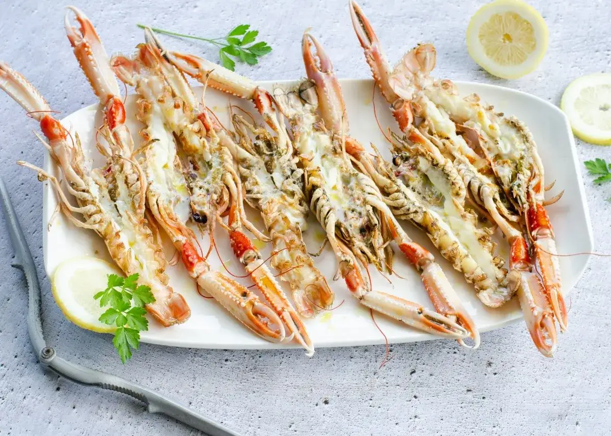 Deliciosas cigalas a la plancha, servidas en una bandeja blanca con rodajas de lim&oacute;n y perejil fresco. Un manjar listo para disfrutar.