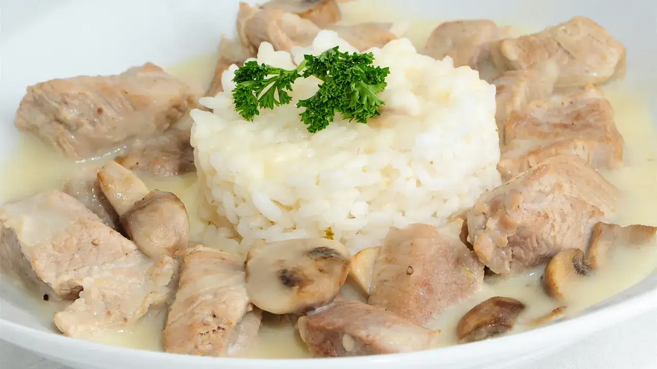 Tiernos escalopines de ternera en salsa cremosa con champiñones y arroz blanco, decorado con perejil fresco.