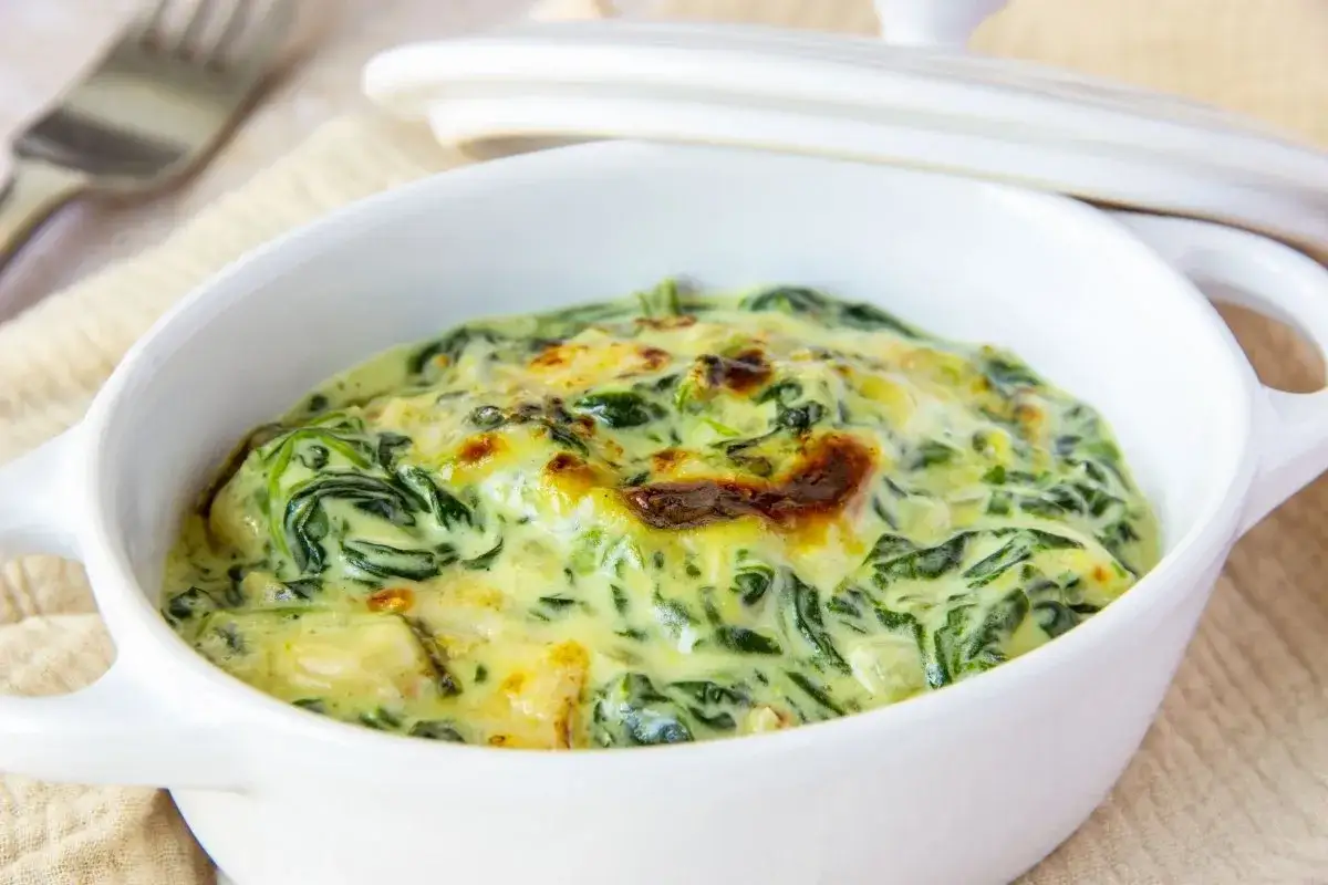 Delicioso plato de espinacas con bechamel gratinada, servido en una cazuela blanca.