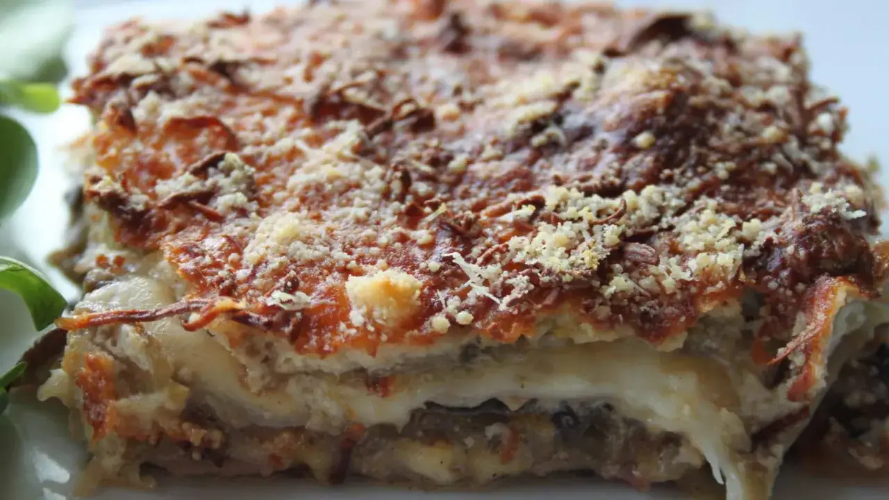 Porci&oacute;n de pastel de berenjenas horneado, con capas de queso derretido y cobertura dorada de pan rallado.