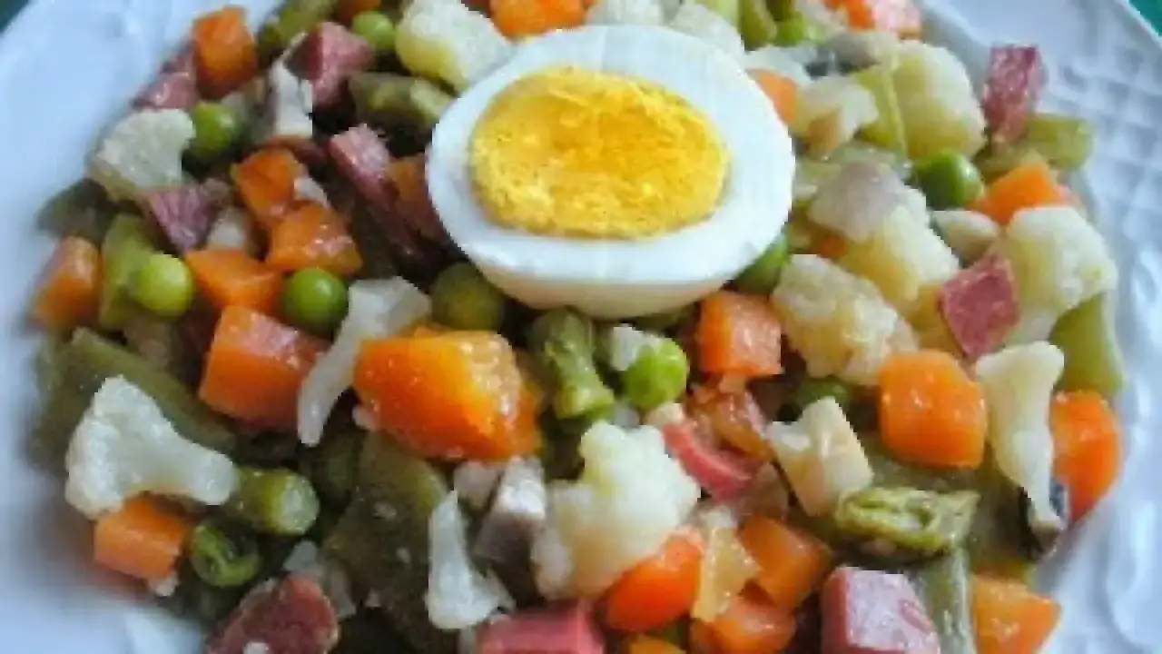 Un plato de menestra de verduras con trozos de zanahoria, patata, judías verdes, guisantes y coliflor, coronado con medio huevo duro.