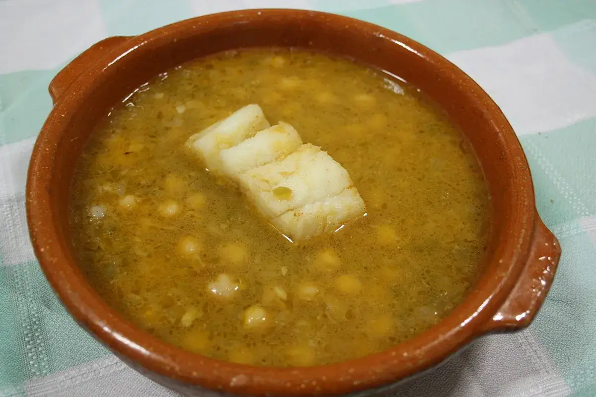 Un reconfortante plato de garbanzos con arroz y trozos de pescado blanco en un cuenco de barro.