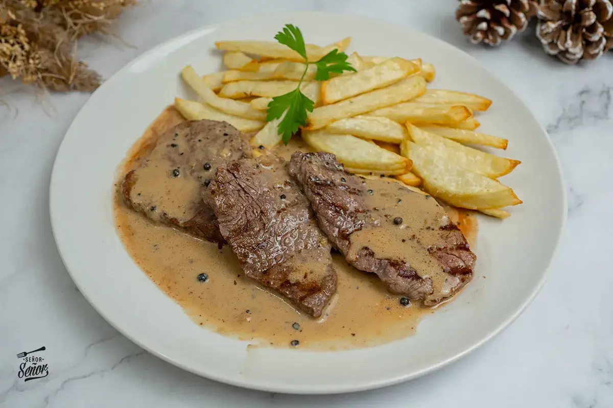 Delicioso solomillo a la pimienta con patatas fritas crujientes. La salsa cremosa y los granos de pimienta negra realzan el sabor de la carne.