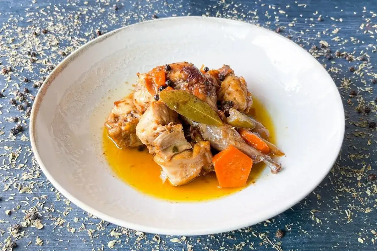 Sabroso conejo en escabeche, con trozos de zanahoria y especias, servido en un plato blanco.