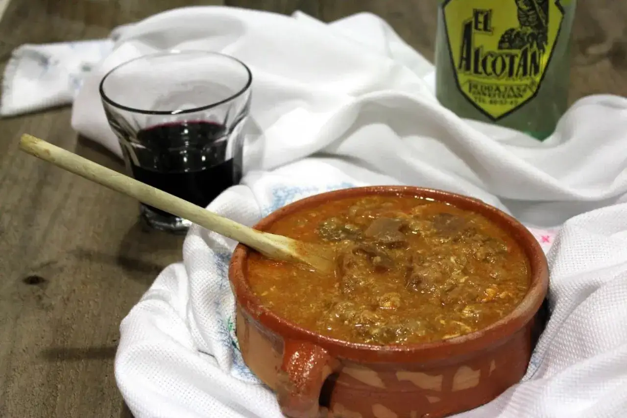 Un cuenco de barro con sopa de ajo, una cuchara de madera, un vaso de vino tinto y una botella de licor. &iexcl;Perfecto para una receta de sopas de ajo!