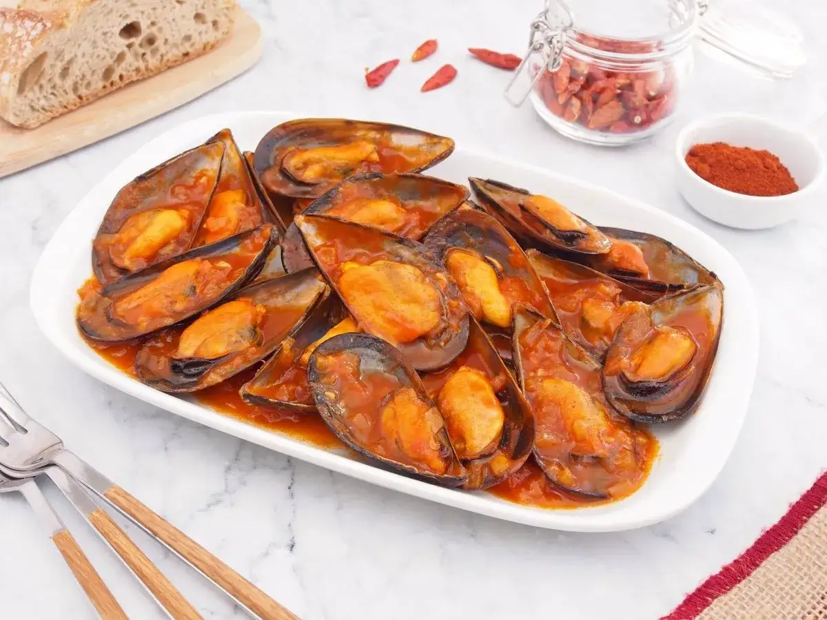 Mejillones en salsa picante, listos para disfrutar con pan rústico y un toque de pimentón.