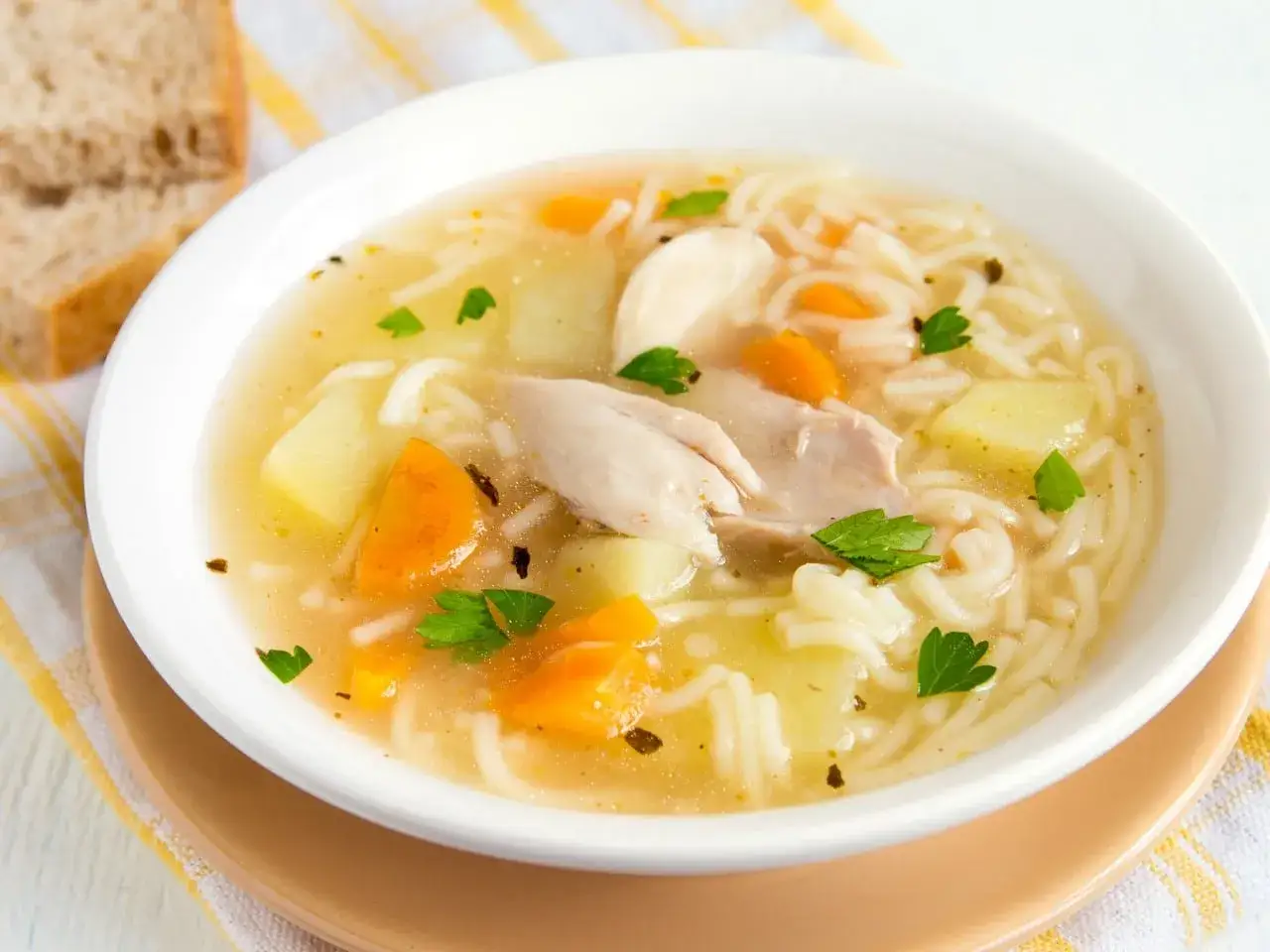 Un reconfortante plato de sopa de pollo con fideos, trozos de zanahoria y patata, adornado con perejil fresco.