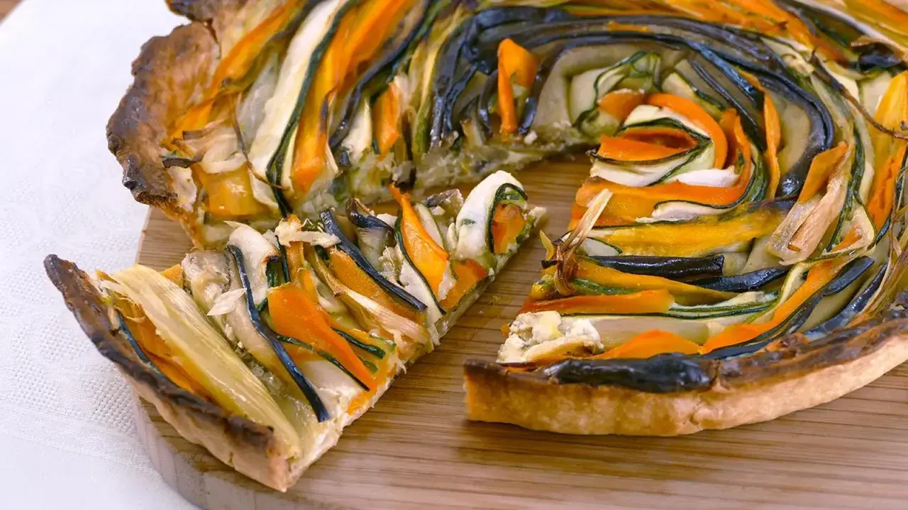 Un colorido pastel de verduras con láminas de calabacín, zanahoria y berenjena dispuestas en espiral sobre una base dorada.