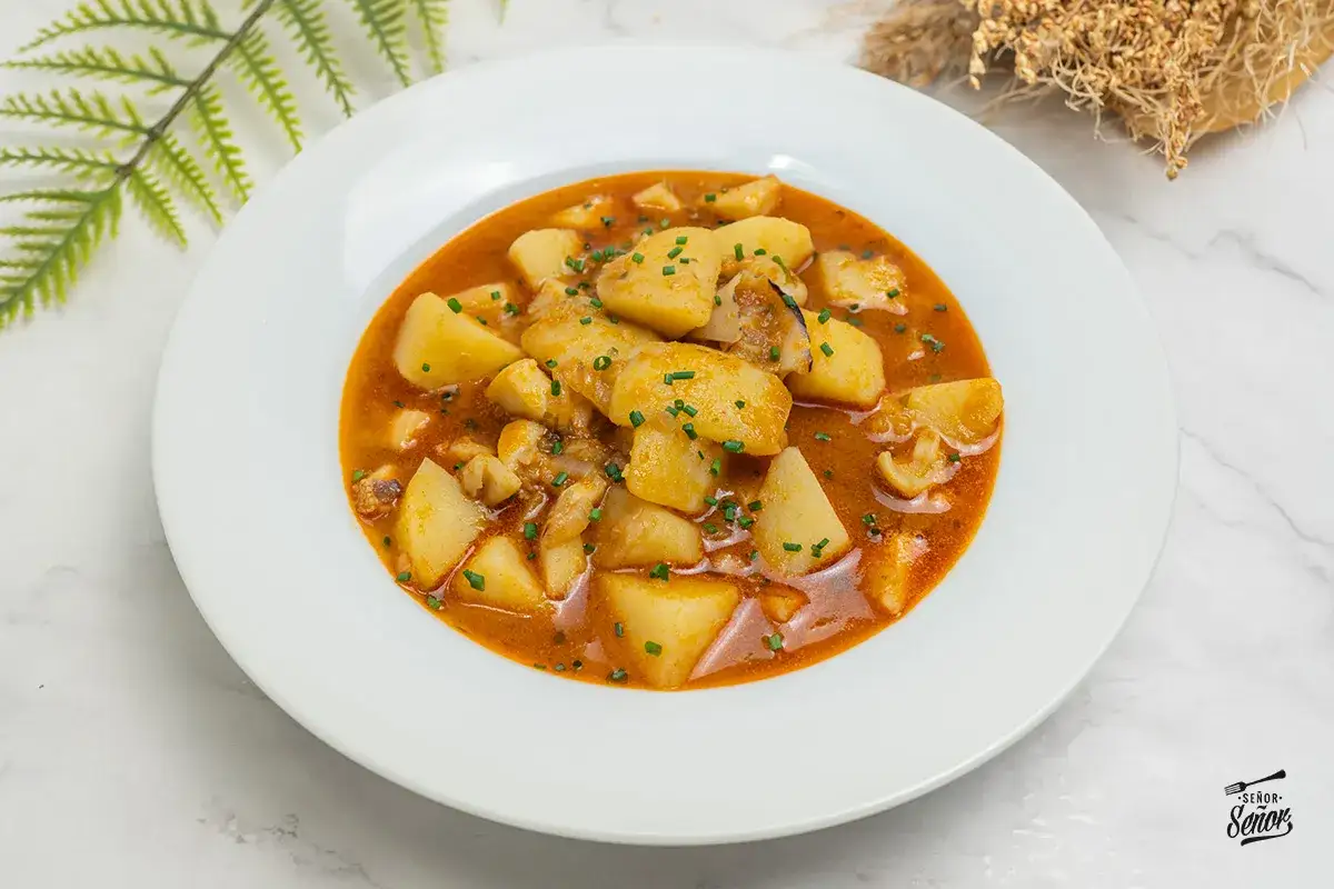 Un plato de sepia con patatas en salsa roja, decorado con cebollino picado.