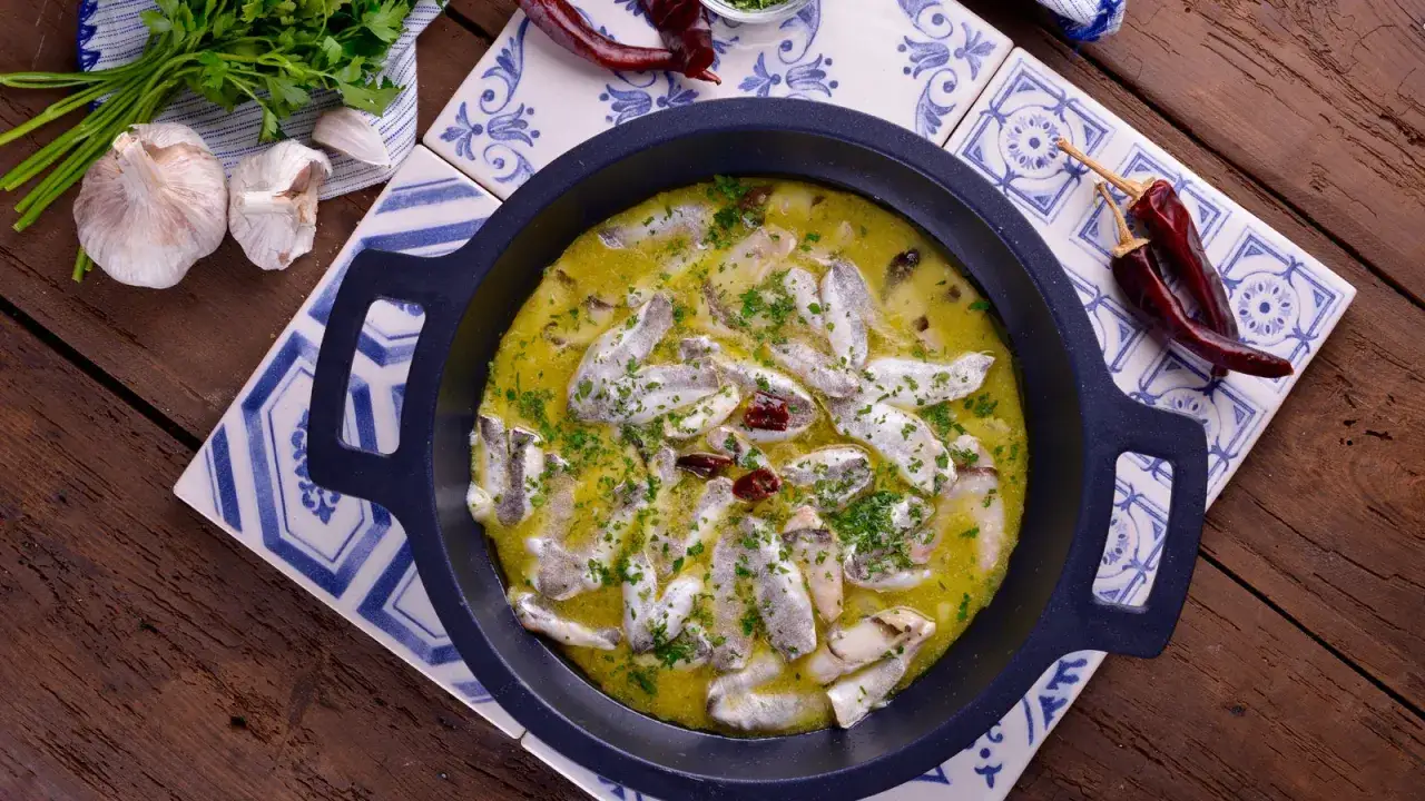 Cocochas de merluza en salsa verde, con ajos, perejil y guindillas secas, servidas en cazuela negra sobre azulejos.