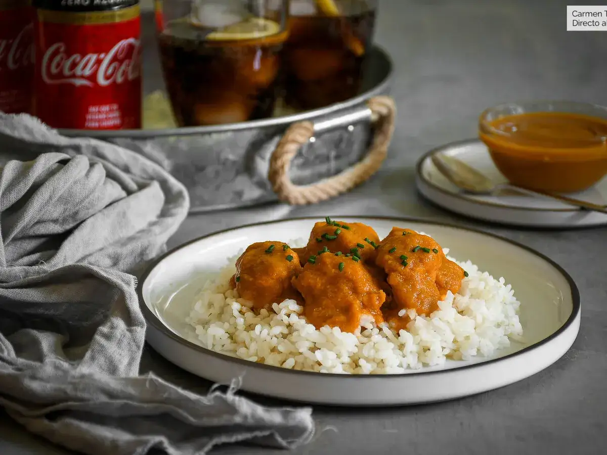 Sabroso pollo a la Coca Cola servido sobre arroz blanco, con latas de Coca Cola y vasos de bebida en el fondo.
