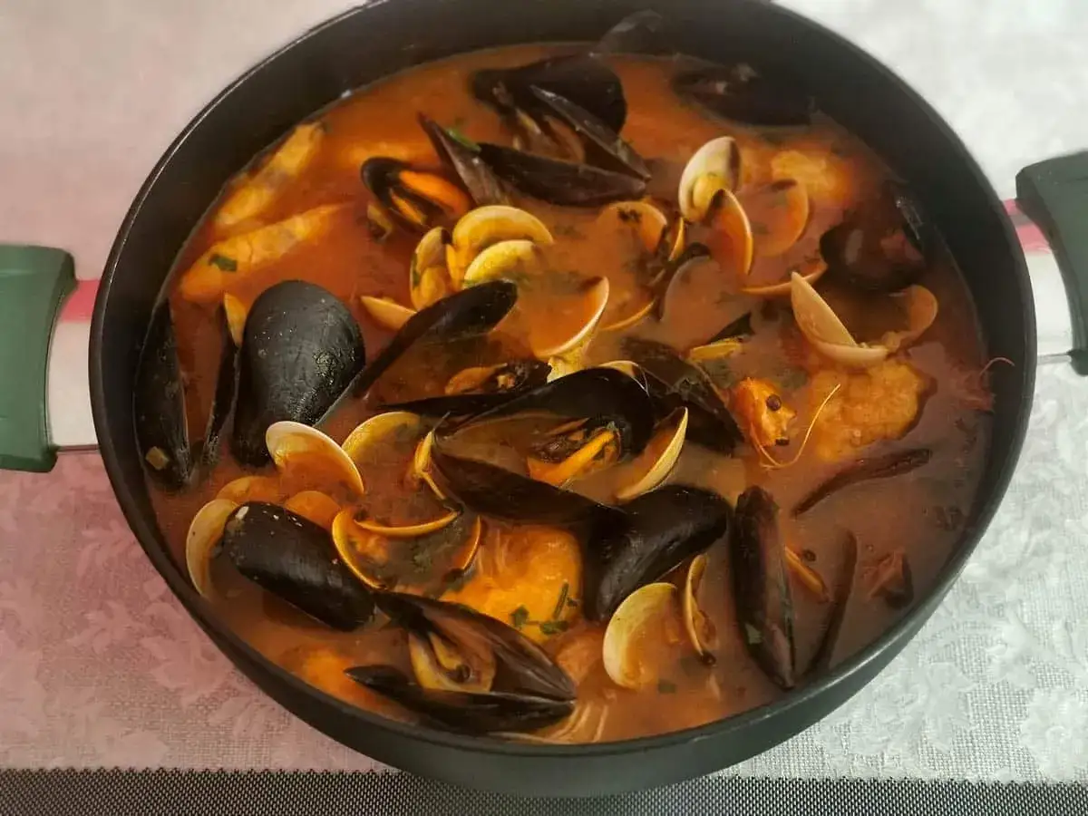 Caldereta de pescado humeante en una olla, repleta de mejillones, almejas y trozos de pescado en una rica salsa roja.