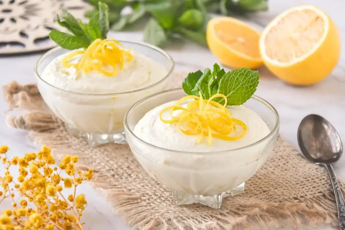 Dos copas de cremoso mousse de limón con leche condensada, decoradas con ralladura de limón y menta.