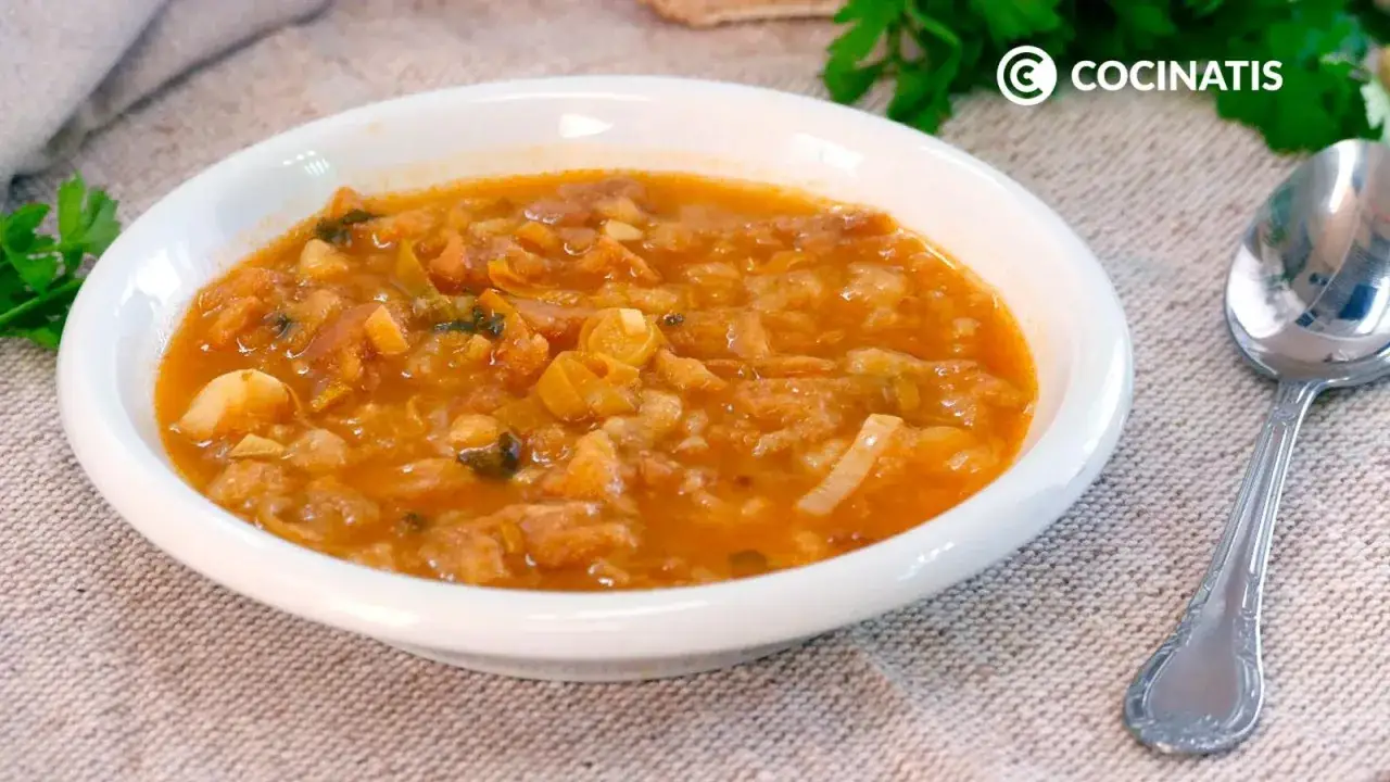 Un plato blanco lleno de una sabrosa sopa de pescado, con trozos de pescado, patatas y verduras.